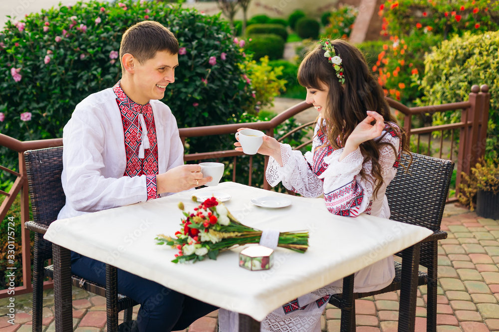 guy and girl in embroidered clothes sitting in cafe and drinking guy and girl in embroidered clothes sitting in cafe and drinking