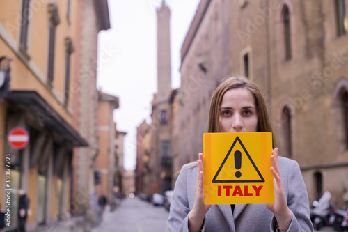 Coronavirus. Girl holds a yellow sign in her hands with the text ITALY. The concept of pandemic and infectious diseases worldwide. Girl on the street of the city of Bologna. Health threat. Copy space photo