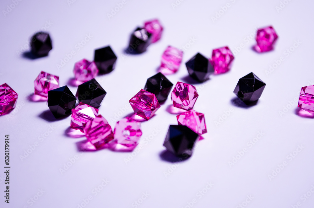 A scattering of beads on a white background, a sheet. Crystals. Iridescent and shiny pink and black beads. Materials for needlework. Style and fashion. For girls and children. Crystals close-up.