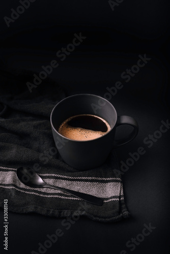 Φωτογραφία Photograph of black coffee cup with coffee foam and black spoon, on black and white cloth