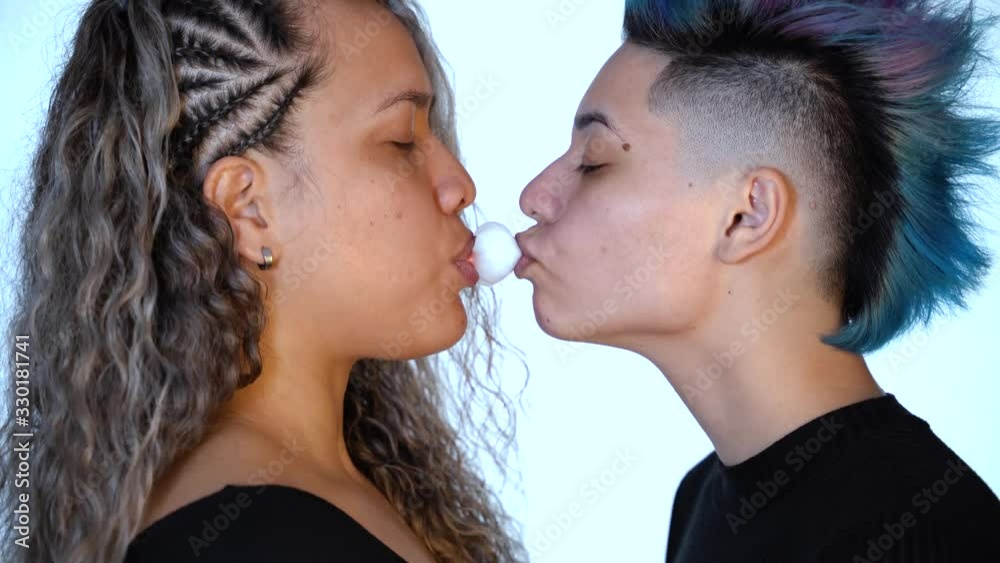Ethnic and punk millennial lesbian couple laughing and playing with a bubble of chewing gum and kissing. Modern gay love. Lgbt and pride concept. Gay lifestyle. Real lesbian couple.