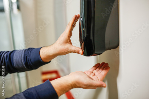 Two Hands under the automatic alcohol dispenser.
