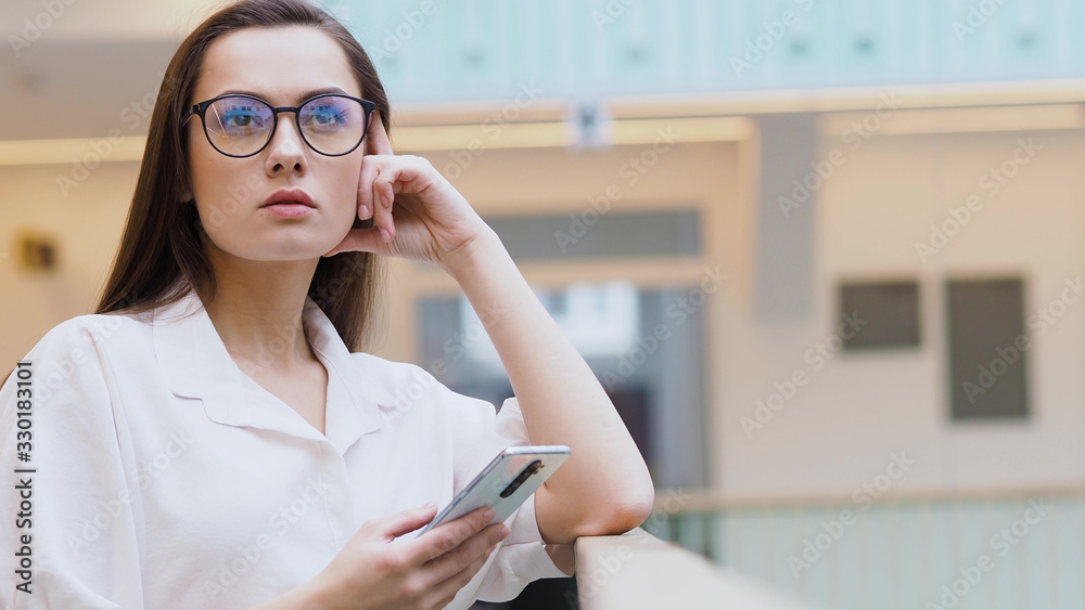 thoughtful young woman in a white shirt and glasses in the interior of a business center.