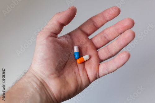 A male hand on a white background holds two capsules of blue and orange
