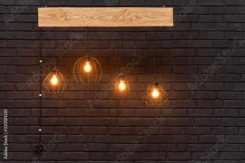 Orange retro lamps hanging on a wooden board on a background of dark black brick wall. Modern template with place for advertisement or text. Light Hanging Interior Design