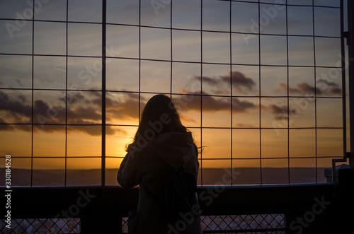 Silhouette of a woman who watches the sunset from a viewpoint