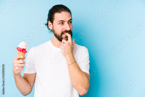 Young caucasian man eating an ice cream isolated relaxed thinking about something looking at a copy space.