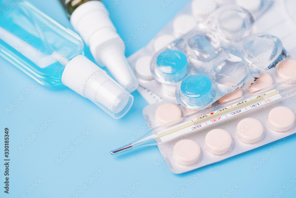 Medical examination and treatment concept. Pills, thermometer, medical mask, spray and antiseptic on a blue background. top view of the background. Medical flat lay Medical examination and treatment concept. Pills, thermometer, medical mask, spray and antiseptic on a blue background. top view of the background. Medical flat lay