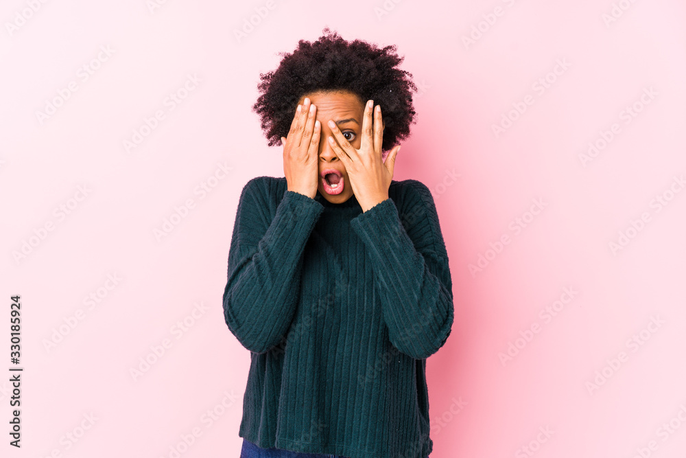 Middle aged african american woman against a pink background isolated blink through fingers frightened and nervous. Middle aged african american woman against a pink background isolated blink through fingers frightened and nervous.