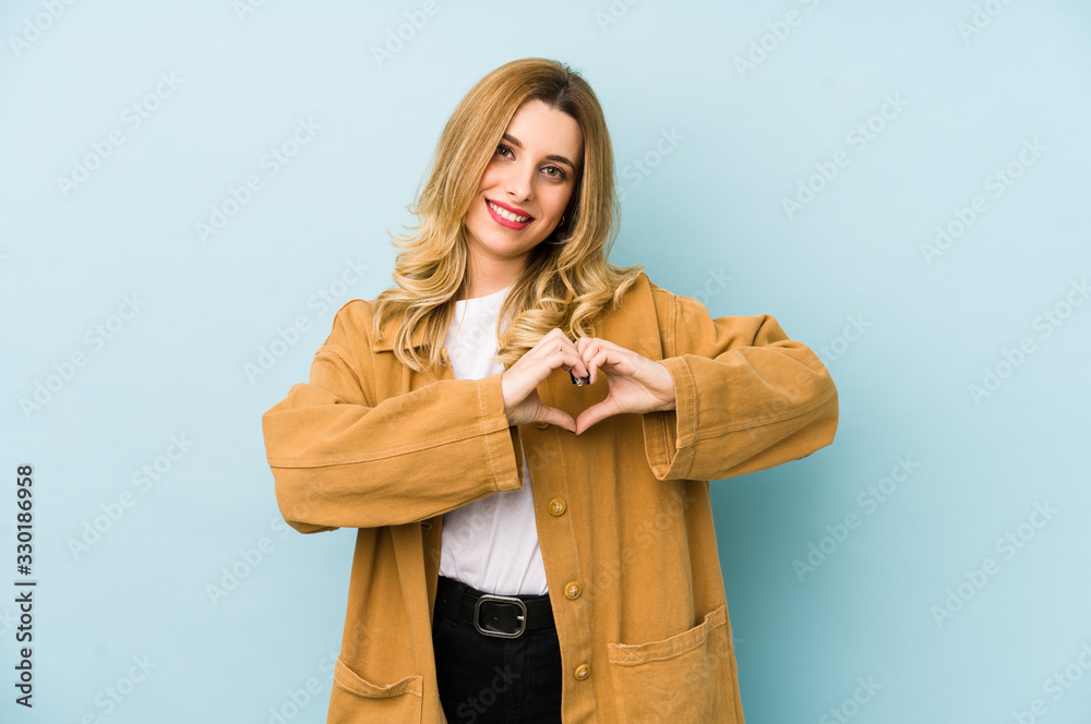 Young blonde pretty woman isolated smiling and showing a heart shape with hands. Young blonde pretty woman isolated smiling and showing a heart shape with hands.