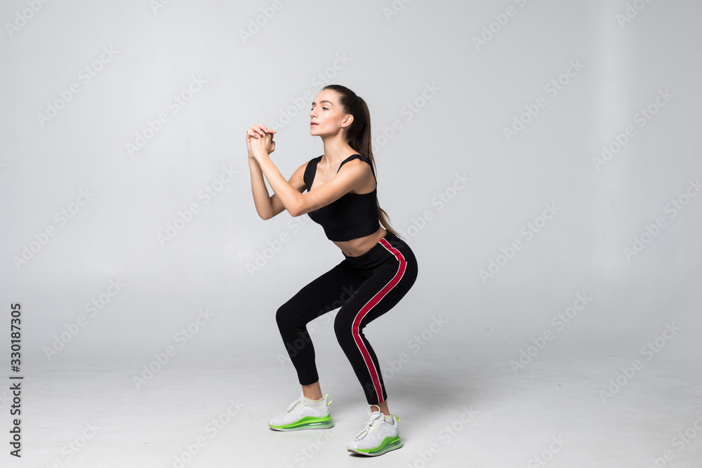 Young smiling sport woman doing squats on gray background Young smiling sport woman doing squats on gray background