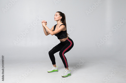Young smiling sport woman doing squats on gray background