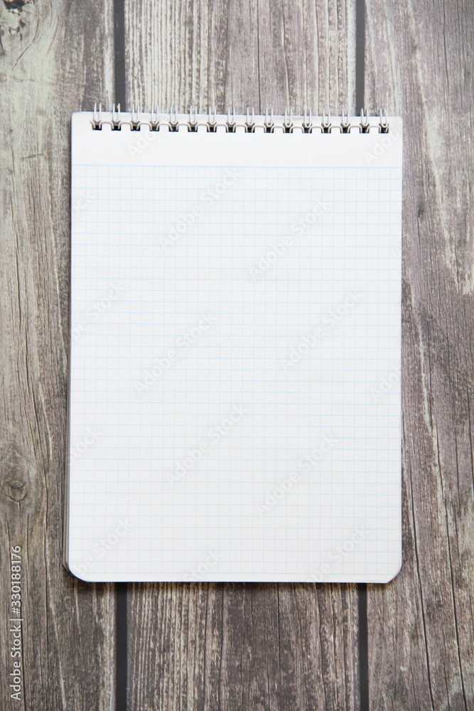 Notepad with a blank white sheet in a checker paper lies on the background of wooden boards. Notepad with a blank white sheet in a checker paper lies on the background of wooden boards.