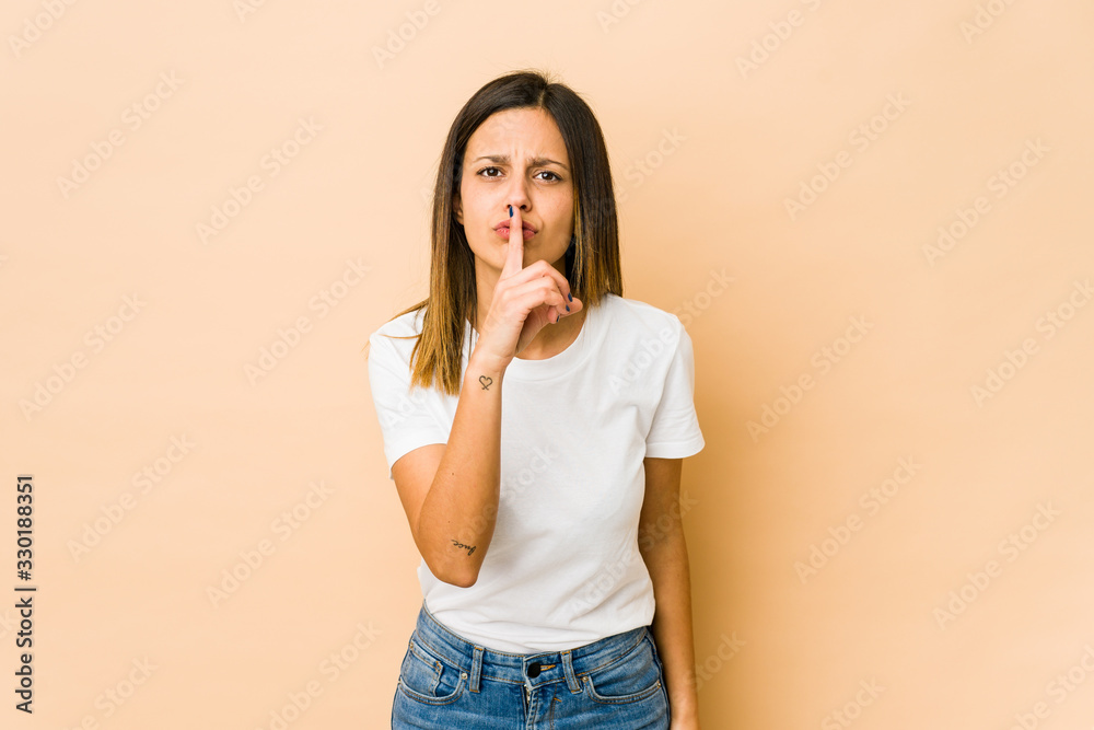 Young woman isolated on beige background keeping a secret or asking for silence. Young woman isolated on beige background keeping a secret or asking for silence.