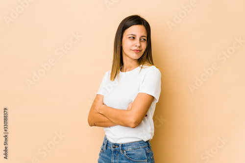 Young woman isolated on beige background suspicious, uncertain, examining you.