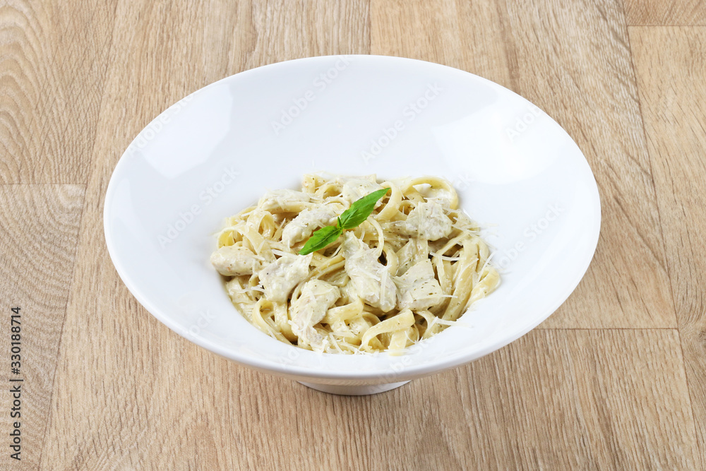 alfredo pasta with basil leaves and Parmesan cheese in a white plate on a wooden background