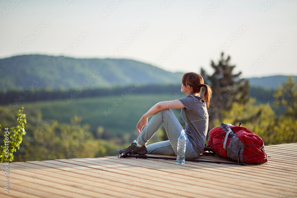 young female sitting on viewpoint high in mountain, looking at distance. nature, relaxing, leisure, filling with energy concept