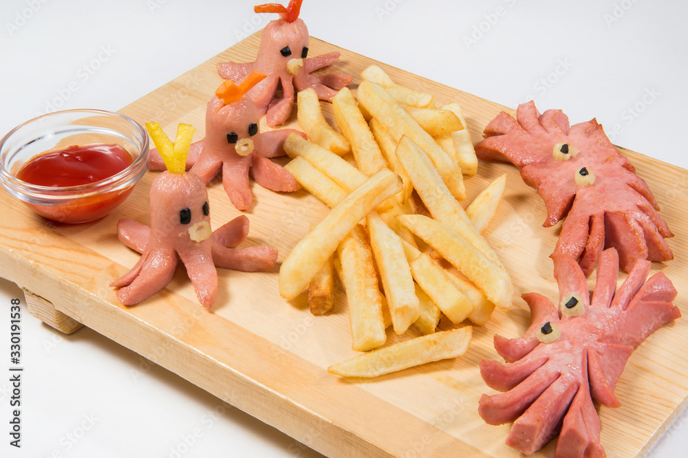 French fries with octopus sausages on a board. Children`s dish on the marine theme. Photographed at an angle of 45 degrees. French fries with octopus sausages on a board. Children`s dish on the marine theme. Photographed at an angle of 45 degrees.