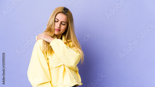Young blonde woman isolated on purple background having a shoulder pain.