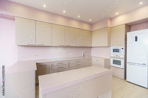 New kitchen furniture  set in white colors in the style of minimalism in a new building. pink wall. kitchen appliances  refrigerator  gas stove with oven. Table in front of the kitchen