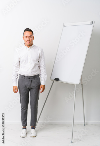 Young latin coaching man with a whiteboard isolated confused, feels doubtful and unsure.