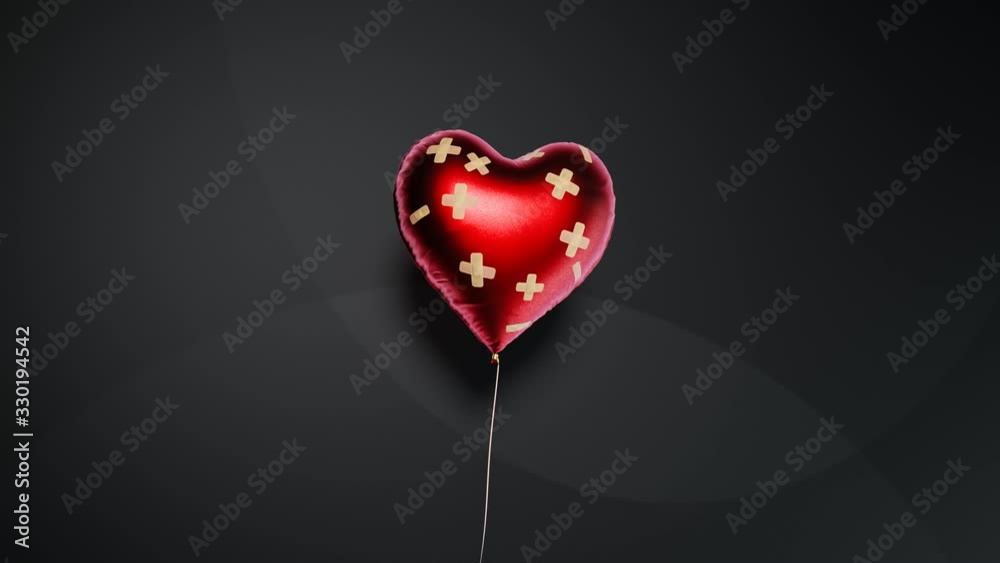 Red heart-shaped balloon fixed with bandaids. Broken heart concept. 4kHD
