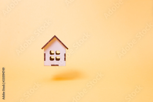 a small wooden decorative house flies on a yellow background, the levitation of the item, the place of the copy, the sale and construction of houses concept