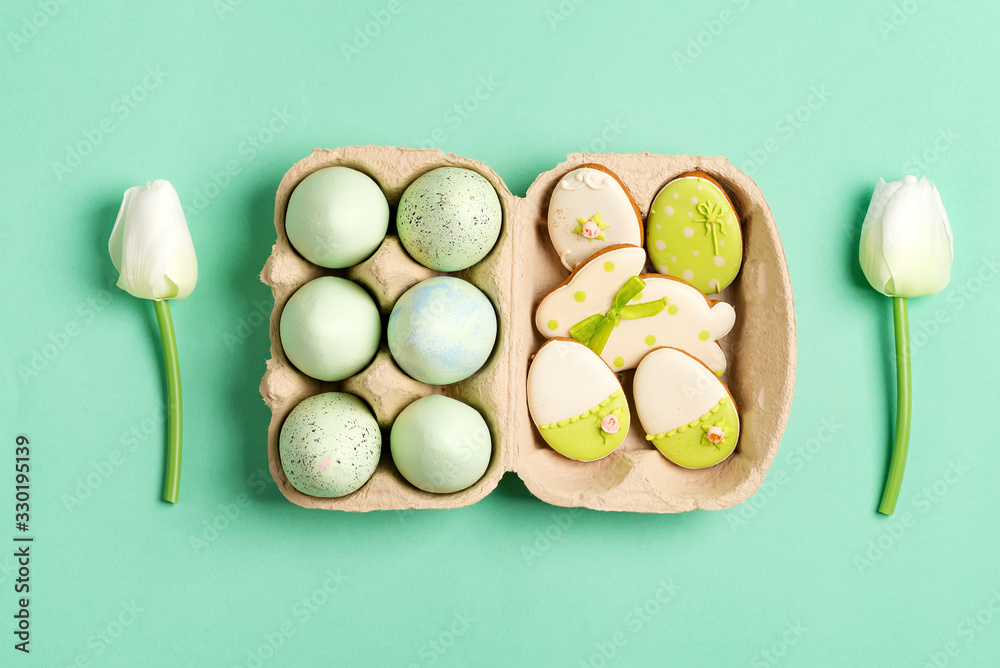 Easter composition from craft painted eggs in paper box, tulips flowers and baked cookies on a green background. Easter composition from craft painted eggs in paper box, tulips flowers and baked cookies on a green background.