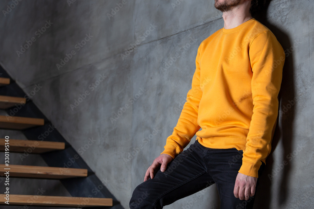 Man in yellow blank sweatshirt or long sleeved. Standing on the stairs near the wall at home. Mockup for print