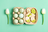 Easter composition from craft painted eggs in paper box, tulips flowers and baked cookies on a green background.