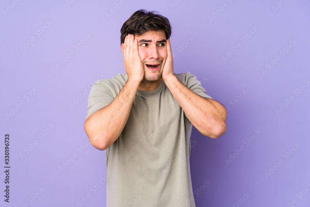 Young man isolated on purple background covering ears with hands trying not to hear too loud sound. Young man isolated on purple background covering ears with hands trying not to hear too loud sound.