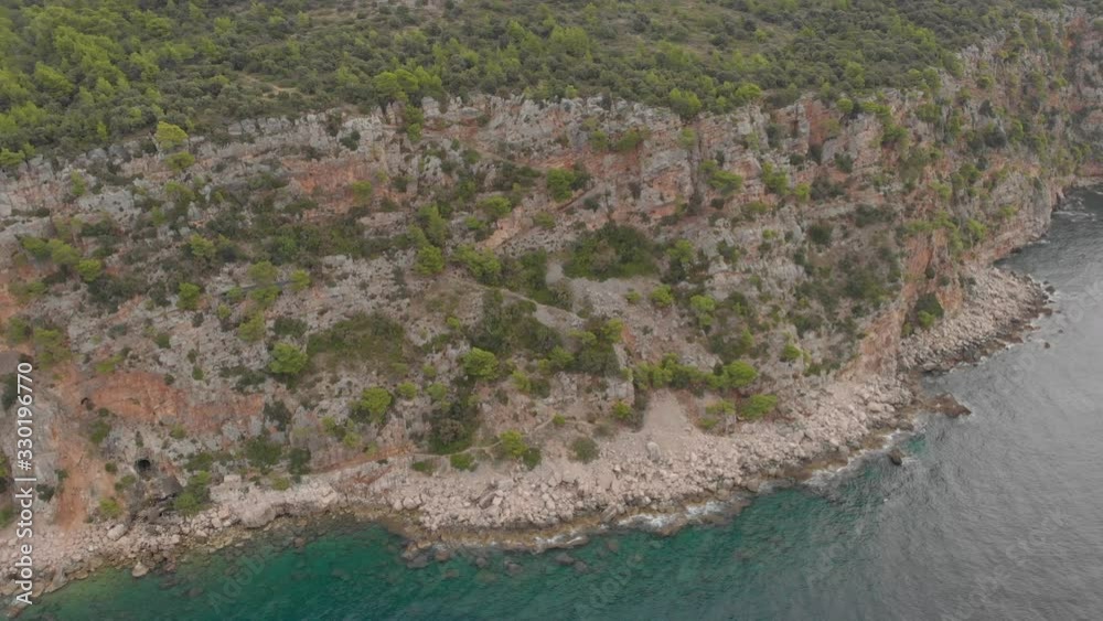 Steep bushy rocks on a sea shore. Cracked cliff with green forest on it's top Steep bushy rocks on a sea shore. Cracked cliff with green forest on it's top