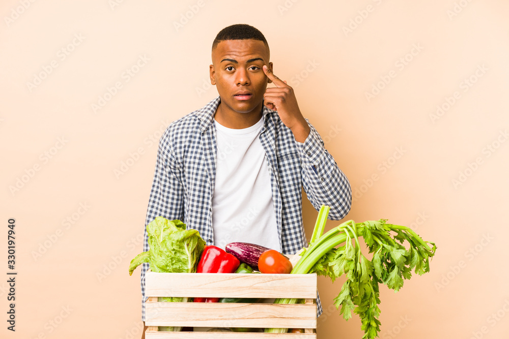 Young farmer man isolated on a beige background showing a disappointment gesture with forefinger. Young farmer man isolated on a beige background showing a disappointment gesture with forefinger.