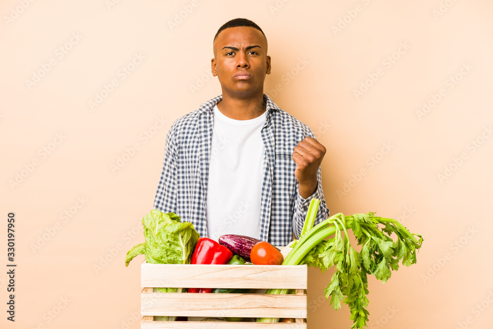 Young farmer man isolated on a beige background showing fist to camera, aggressive facial expression. Young farmer man isolated on a beige background showing fist to camera, aggressive facial expression.