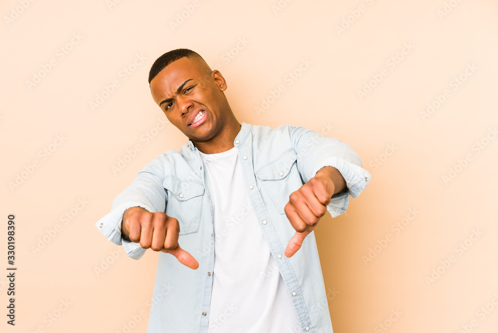 Fototapeta premium Young latin man isolated on beige background showing thumb down and expressing dislike.