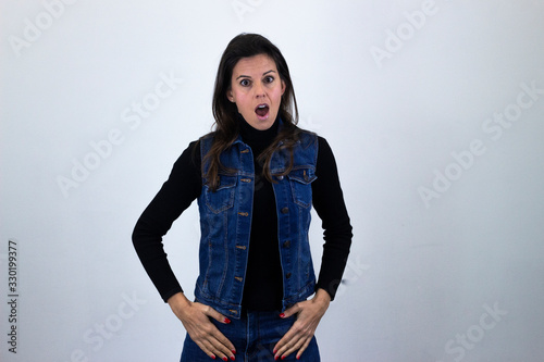Portrait of caucasian middle age woman with stunned expression, keeps mouth opened, isolated on gray background studio shot, black sweater, denim jacket, jeans. Place for your text in copy space.