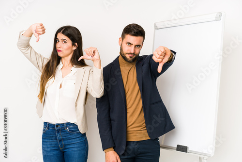 Young caucasian business couple isolated showing thumb down and expressing dislike.