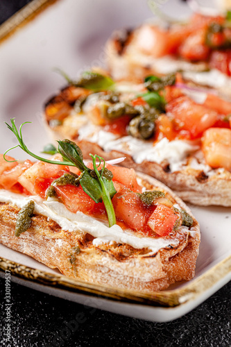 Italian cuisine, antipasti and tapas. Bruschetta of baguette and cottage cheese, tomato, capers, pesto. Serving dishes in a restaurant in white plate. background image, copy space