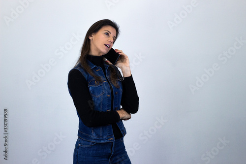 Portrait of attractive caucasian middle age woman talking on mobile phone, isolated on gray background studio shot, black sweater, denim jacket, jeans, dark air. Place for your text in copy space.