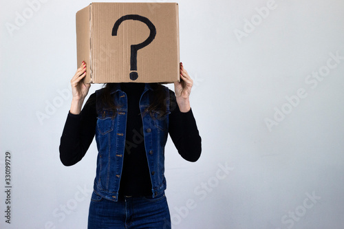 Portrait of attractive caucasian middle age woman with a box on the head and a question mark, isolated on gray background studio shot, black sweater, denim jacket, jeans. Place for your text in copy s