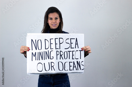 attractive  middle age woman activist hold up protesting sign saying "No deep sea mining protect our oceans" isolated on gray background studio shot, dark air. Place for your text in copy space.