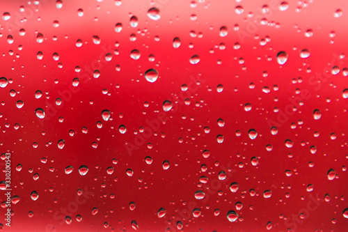 Water droplets from a rain shower on glass with a red background.