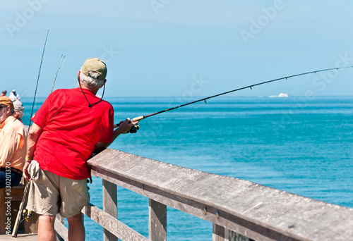 Back view, medium distance of a senior male in red shirt fishing off a wood pier in tropical, gulf of mexico on a sunny, winter day