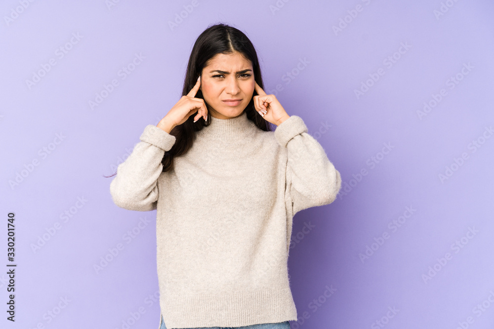 Young indian woman isolated on purple background covering ears with fingers, stressed and desperate by a loudly ambient. Young indian woman isolated on purple background covering ears with fingers, stressed and desperate by a loudly ambient.