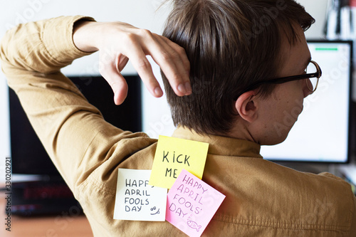 April 1st Fools' day.Man in glasses with  sticker.Sticker on back.Displeased face of man on white background.Office worker.Funny day.Raffle.Kick me.Surprised man.Emotions of a man. Office joke.