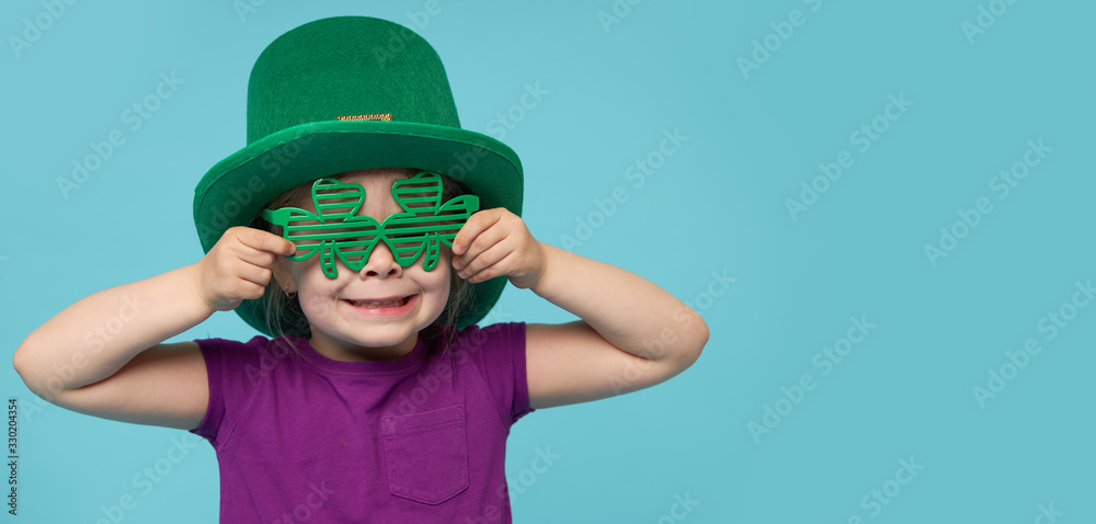 Funny little child girl in green Patricks hat with clover glasses on color background. St. Patricks Day celebration. Advertising space