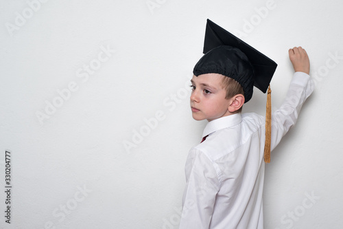 Boy in a student hat writes on the blackboard. White background, copy space. Education concept photo