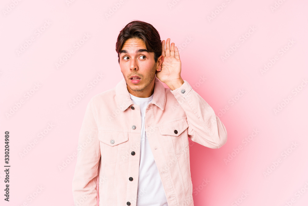 Young caucasian man posing in a pink background isolated trying to listening a gossip. Young caucasian man posing in a pink background isolated trying to listening a gossip.