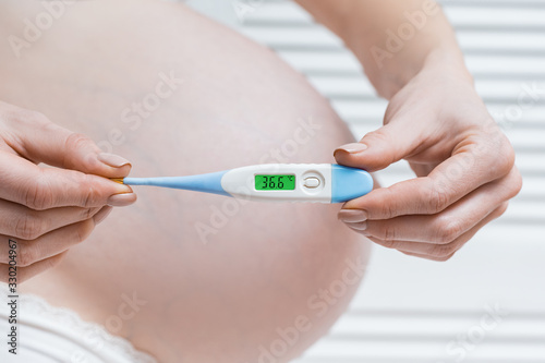 Pregnant woman holding electronic thermometer with normal temperature. Health during pregnancy.