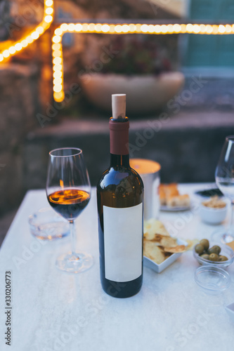 Bottle of red wine and glass on the table, chips, olives, served at restaurant. Soft colours, Summer time, Italy. Copy Space For Text. Tellaro, Ligurian province, Italy. photo